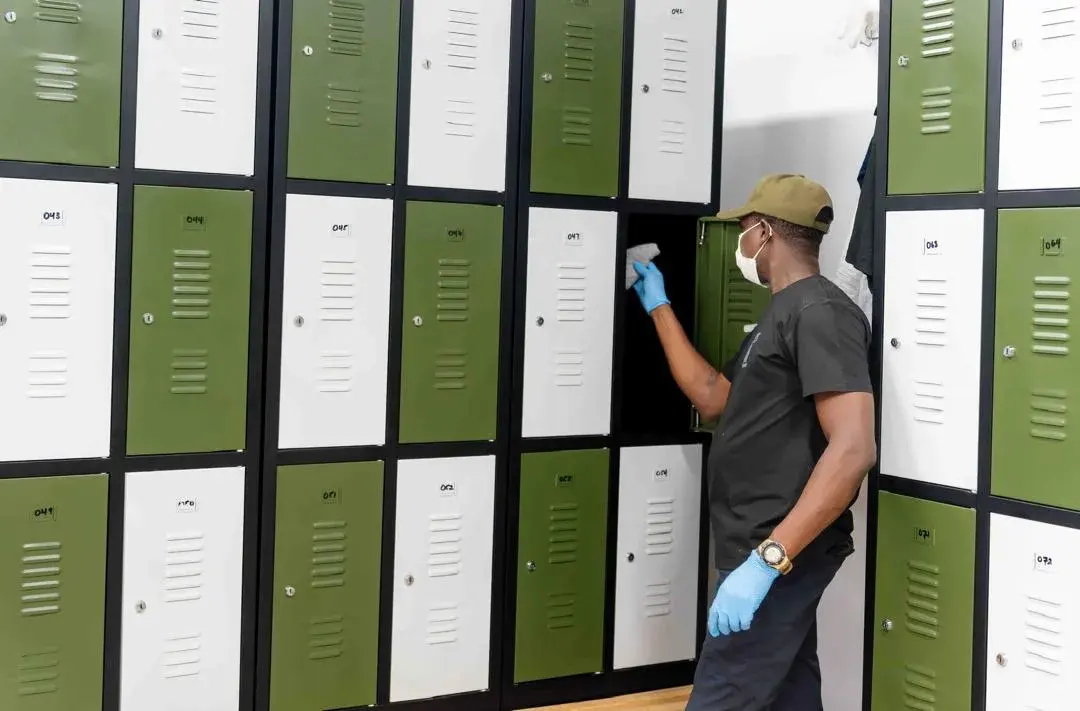 A Clean by AK cleaner wiping the inside of a locker in a changing room